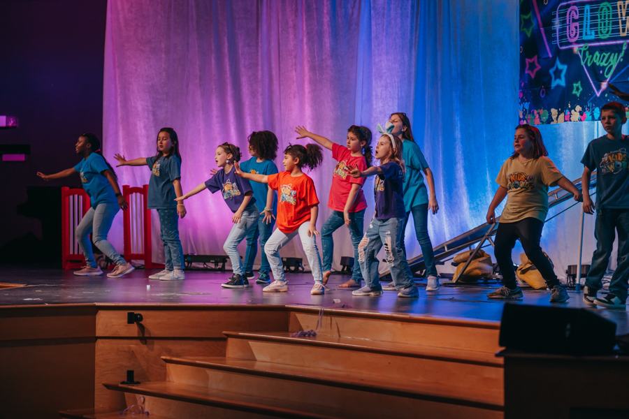 A line of kids performing on stage under coloured lights at Easter Blast