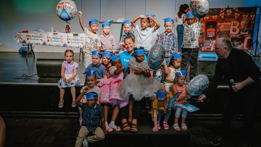 Kids celebrating together on stage with balloons and blue hats